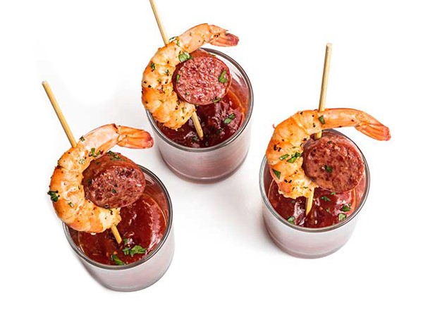 Three shrimp and sausage skewers each served in a cup of sauce