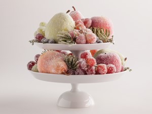 Two white cake stands piled on top of each other holding sugar-coated assorted fruit