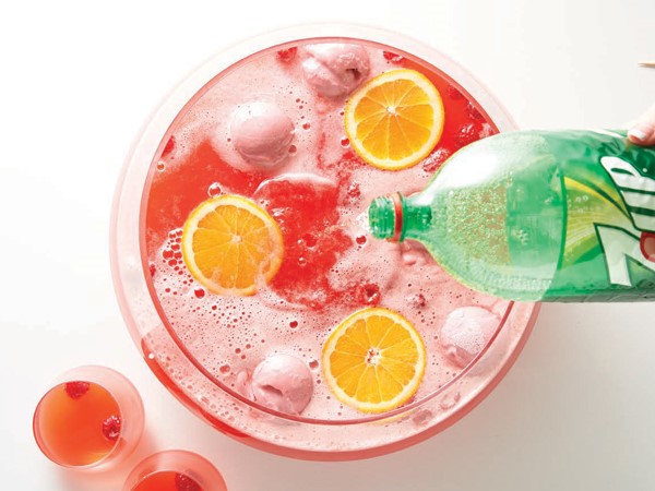 7UP poured into punch bowl with red punch and garnished with orange slices