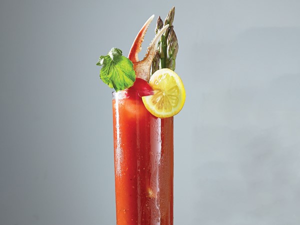 Tall glass of bloody mary, garnished with aspargus, crab leg, lemon slice, cherry tomato and celery stalk