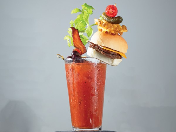 Glass of all-American bloody mary garnished with a cheeseburger, celery stalk, kalamata olives and bacon