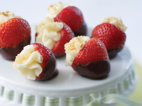 Strawberries partially dipped in dark chocolate and stuffed with cheesecake filling on a white cake stand