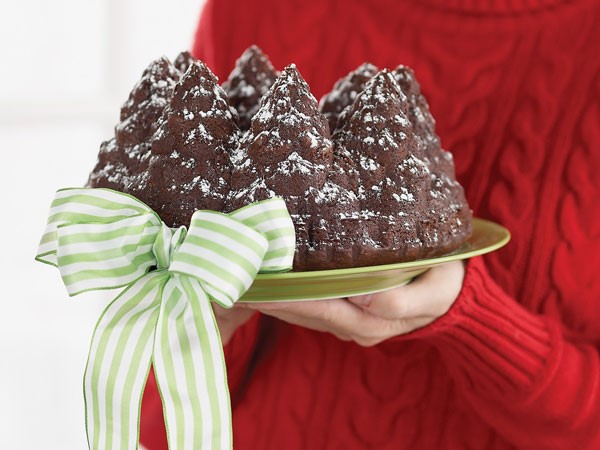 Person in a red sweater holding green platter of chocolate bundt cake with a big green-and-white striped ribbon on it