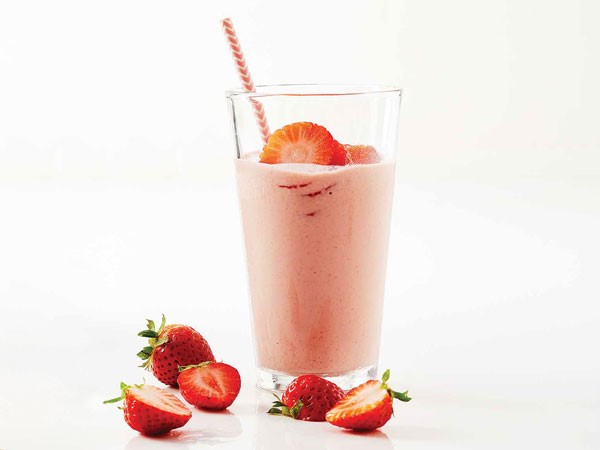 Glass of strawberry cherry workout smoothie garnished with strawberry slices and straw