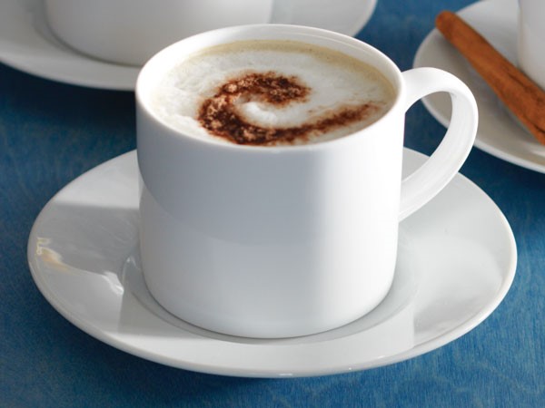 White mug of chocolate almond cafe topped with foam and cinnamon and served with a cinnamon stick