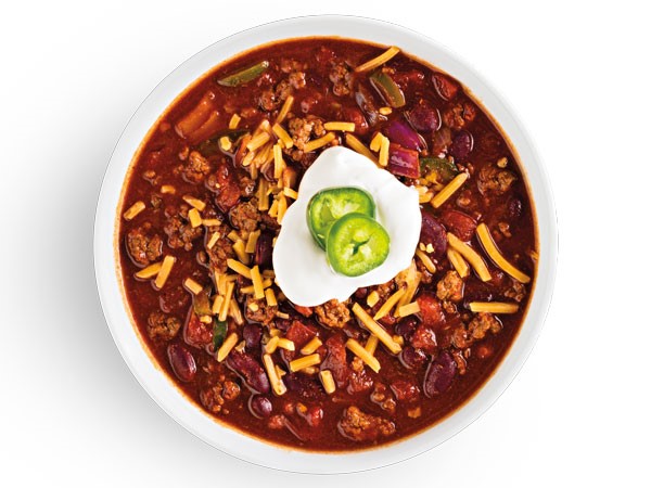 Cup of chili topped with cheddar cheese, dollop of sour cream and jalapeno slices