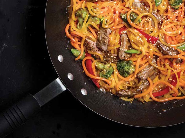 Stir-fry in wok filled with noodles, broccoli, red peppers, water chestnuts, and thinly sliced steak
