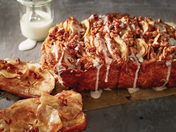 Apple pull apart bread topped with pecans and icing on parchment paper