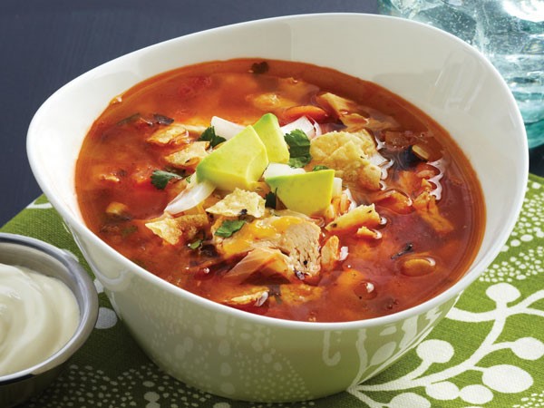 Bowl of soup garnished with tortilla chips and avocado chunks