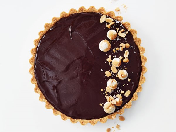 Peanut butter chocolate tart topped with crushed peanuts and whole hazelnuts