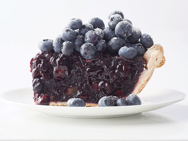 Slice of blueberry pie on a plate topped with fresh blueberries