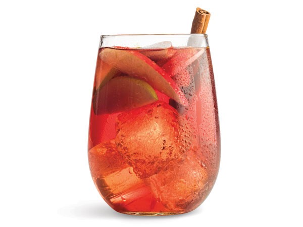 Glass of apple sangria with ice cubes, apple slices and a cinnamon stick