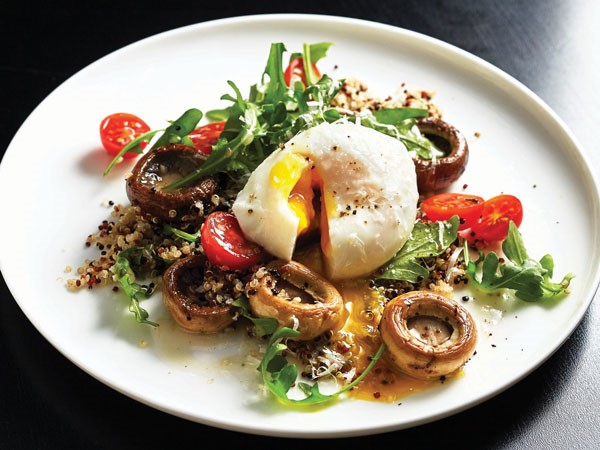 Plate of arugula and grain salad topped with baby bella mushrooms and a poached egg sprinkled with black pepper