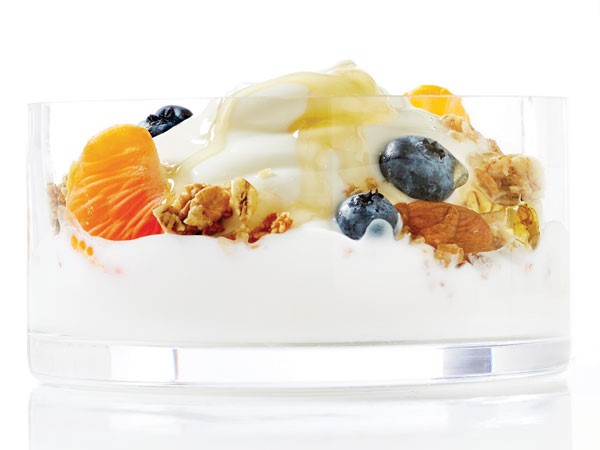 Bowl of yogurt topped with mixed nuts, oranges, honey and blueberries