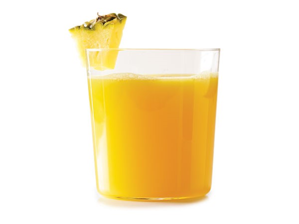 Glass of orange liquid garnished with a pineapple wedge