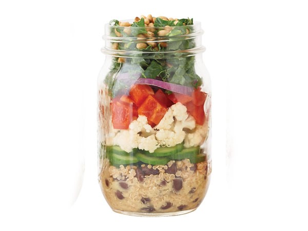 Mason jar layered with quinoa and beans, cucumber slices, cauliflower, bell pepper, red onion, kale and pine nuts