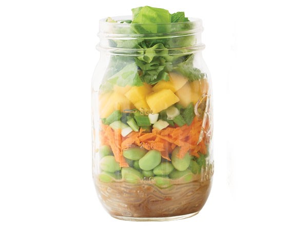 Glass jar layered with peanut butter, edamame, carrots, green onions, mango, lettuce and dressing 