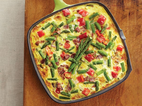 Skillet of frittata mixed with bacon, asparagus, red bell pepper, onion, cheese and parsley