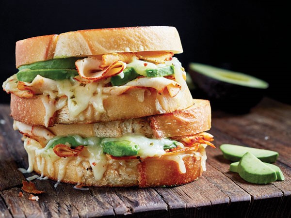Two stacked buffalo chicken sandwiches with sliced turkey, avocado, melted cheese, and buffalo sauce