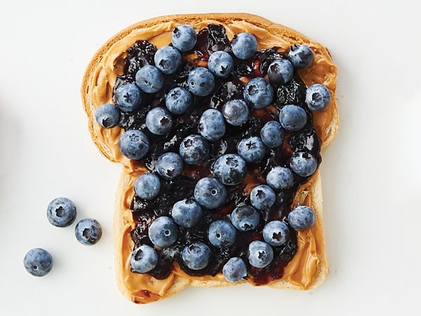 Bread topped with peanut butter, jelly, and fresh blueberries