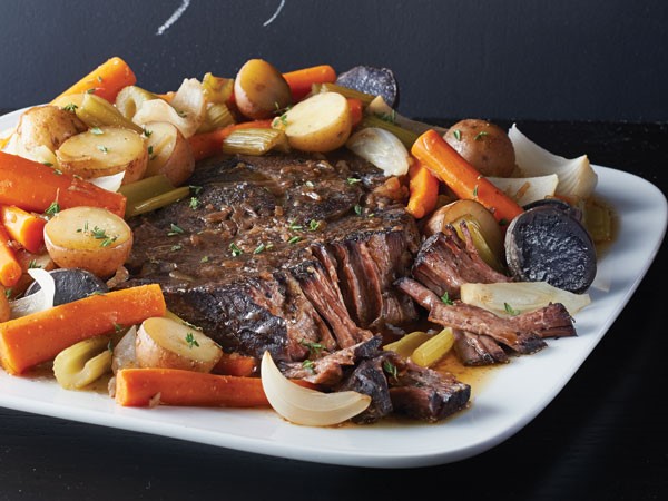 Pot roast surrounded by stewed vegetables on white platter