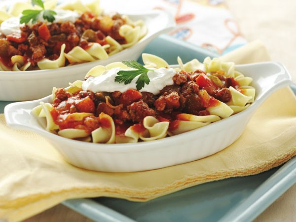 White dish of goulash topped with sour cream and cilantro