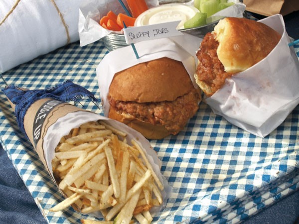Sloppy joe sandwiches served with fries and vegetables on a blue-and-white checkered picnic blanket