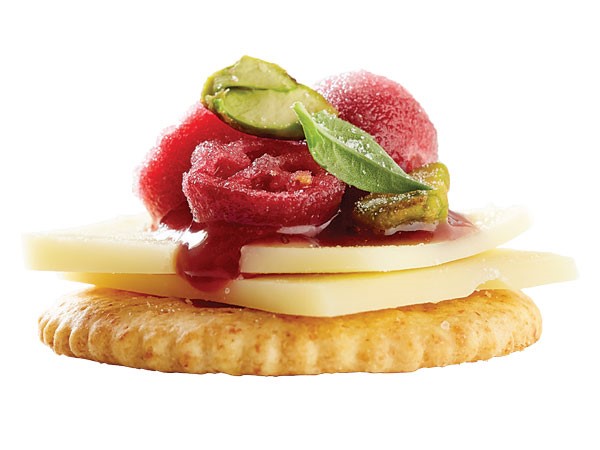 Cracker topped with cheese slice, raspberry jam, pistachios, candied cranberries and mint leaf