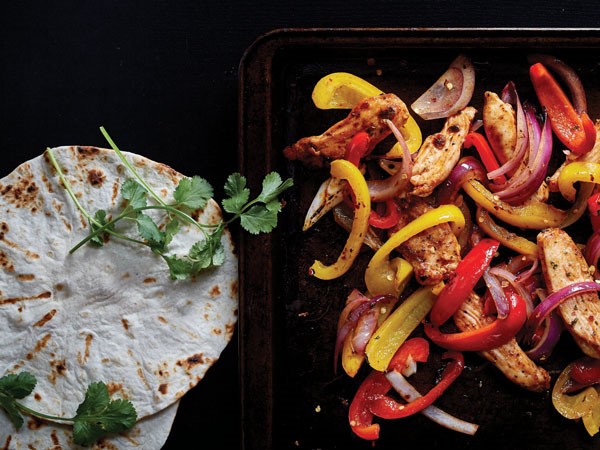 Pan of fajita-seasoned chicken and vegetables served with soft shell tortillas and cilantro