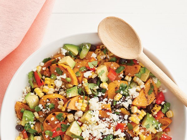 Bowl of grilled sweet potato and corn salad with bell peppers, beans, avocado, green onion, jalapenos, cilantro and cotija cheese