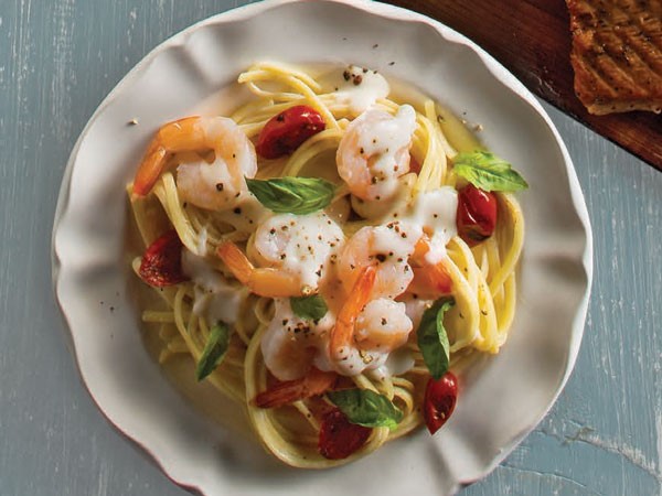 Plate of linguine pasta mixed with creamy alfredo and topped with shrimp, basil and grape tomatoes