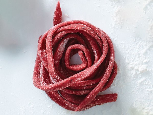 Clump of beet pasta strands dusted with flour