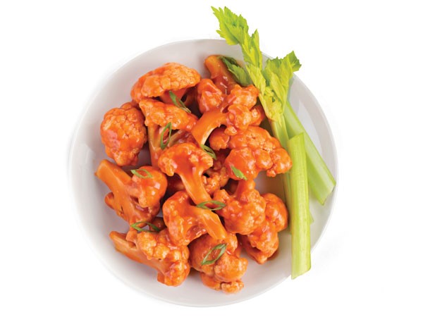 Plate of cauliflower bites covered in buffalo sauce served with celery