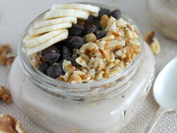 Mason jar filled with overnight oatmeal, topped with sliced bananas, chocolate chips and walnuts