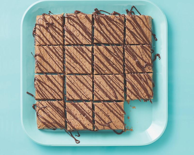 Blue tray of chocolate-peanut butter protein bars drizzled in chocolate with one missing square