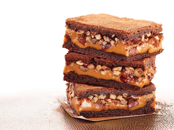 Caramel-pecan brownies stacked on parchment paper