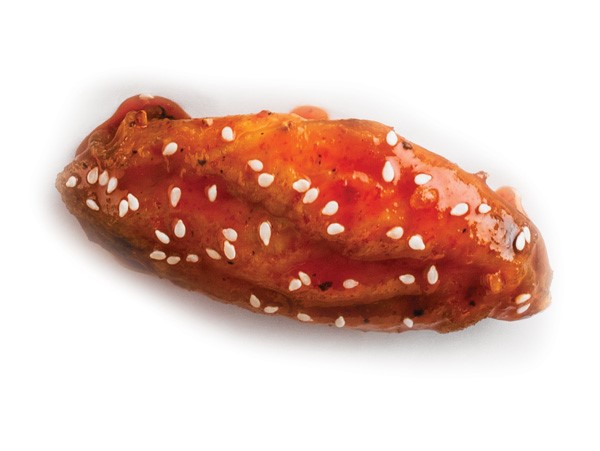 Chicken wing coated in sriracha sauce and sprinkled with sesame seeds
