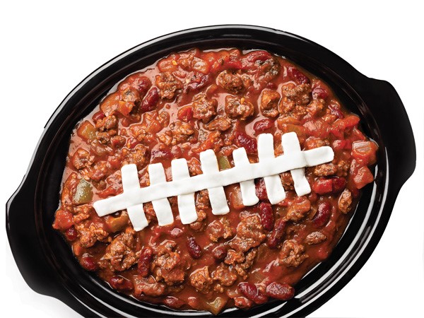 Slow-cooker filled with beef and bean chili with piped sour cream football lace down the center of the dish