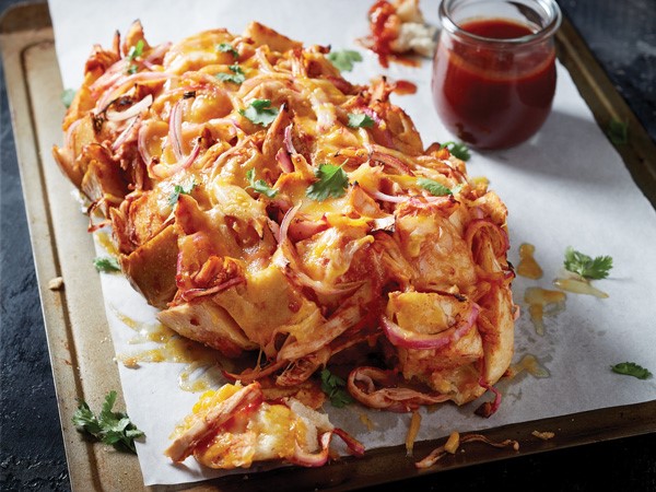 Tray of BBQ chicken pull apart pizza topped with cheese, onion and cilantro