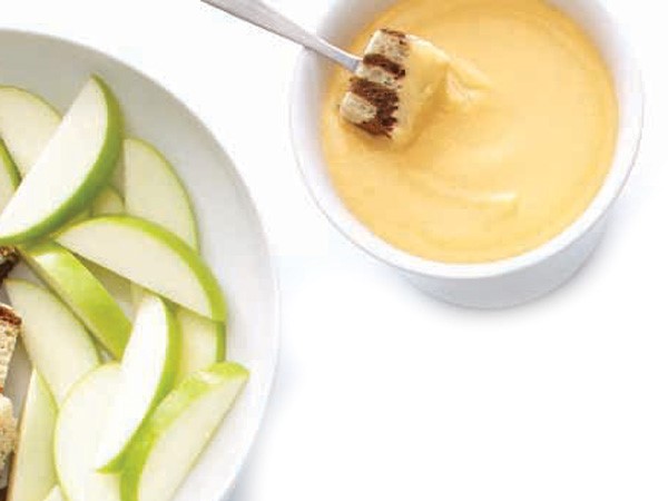 Cubed Bread dipped into Cheese Fondue next to plate of sliced green apples