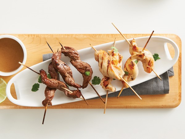 White platter of beef and chicken satay on wooden skewers garnished with cilantro
