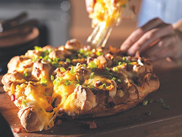 Wooden plank of cheesy monkey bread topped with green onions and bacon bits