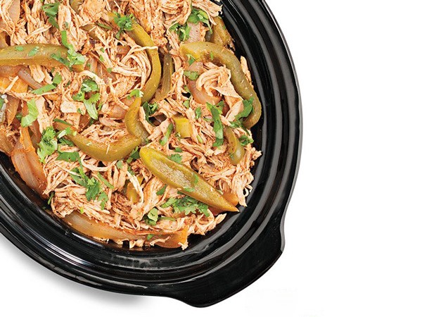 Slow cooker filled with chicken fajita meat and garnished with sliced green bell peppers and cilantro