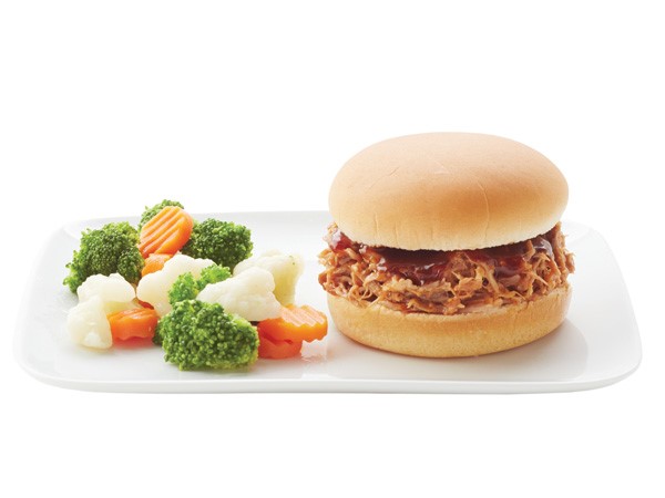 BBQ pulled pork sandwich on a white plate with veggies