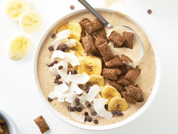 Smoothie bowl topped with mini chocolate chips, coconut flakes, banana chips, and chocolate cereal