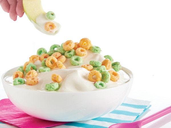 Apple slice dipped into fruit dip topped with Apple Jacks