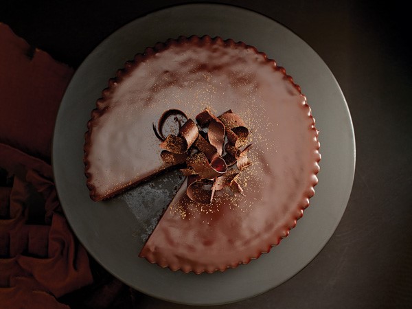 Chocolate truffle tart topped with cocoa powder and chocolate shavings with slice cut out
