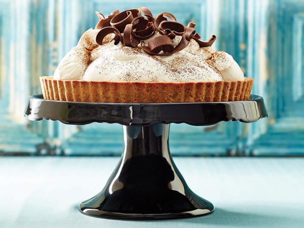 Coffee cream chocolate tart garnished with cocoa powder and chocolate shavings on a cake stand