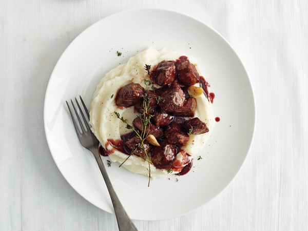 Plate of steak tips served over a bed of mashed parmesan potatoes