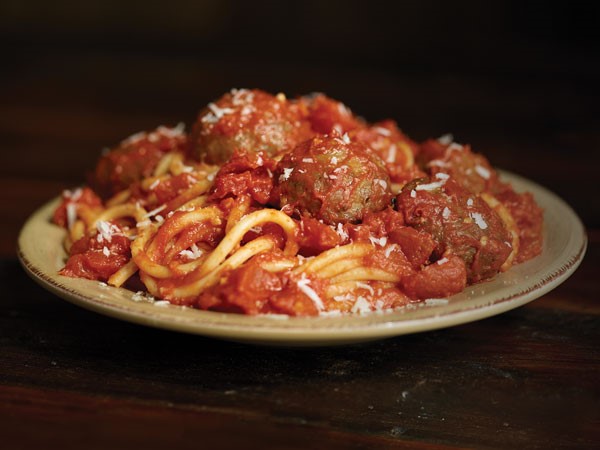 Plate of bucatini pasta topped with tomato pasta sauce and meatballs